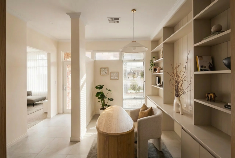 A bright, modern home office with a large wooden desk, comfortable armchair, and built-in shelving.