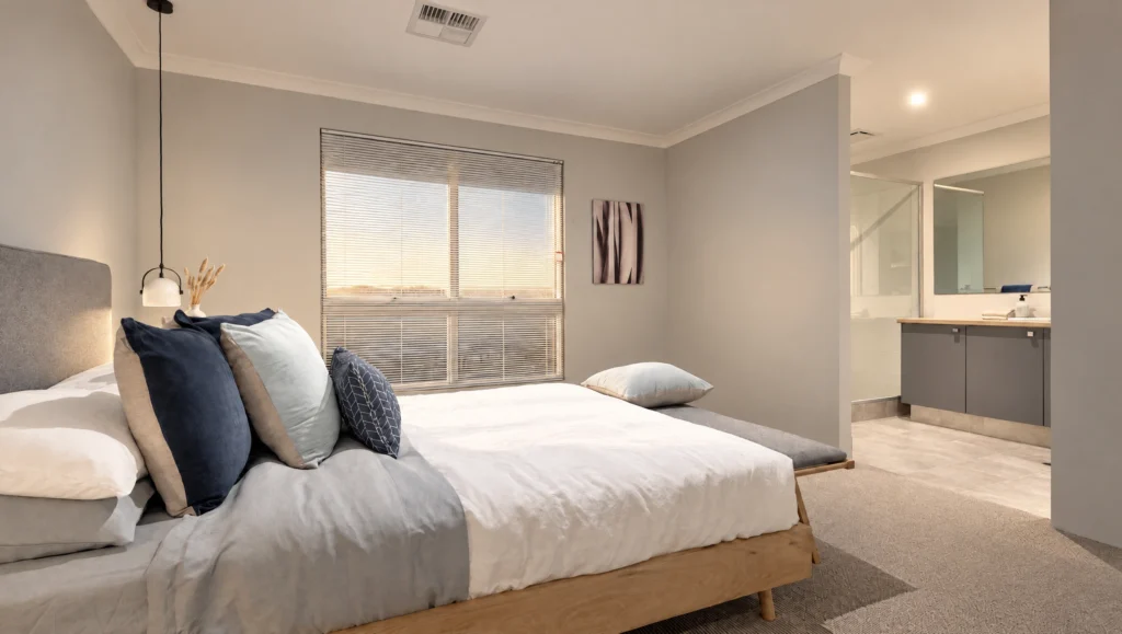 The Eagle Bay bedroom features a king-size bed with blue and grey pillows, a window with blinds, and an ensuite bathroom.
