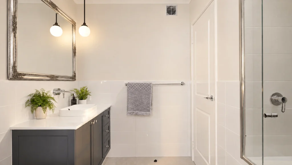 Modern bathroom with a dark vanity, white countertop, vessel sink, ornate mirror, and glass shower.