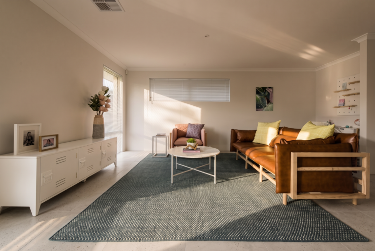 A modern living room with a tan leather sofa, pink armchair, white coffee table, and a white console table.