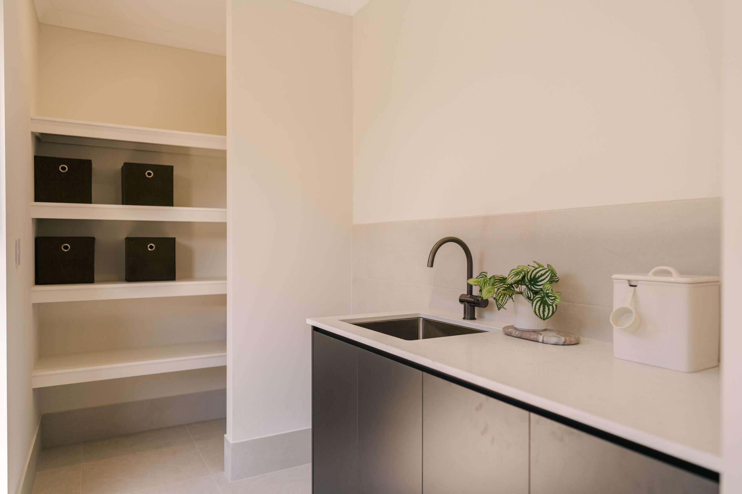 Modern laundry room with a dark faucet, white countertop, and built-in shelving with storage boxes.