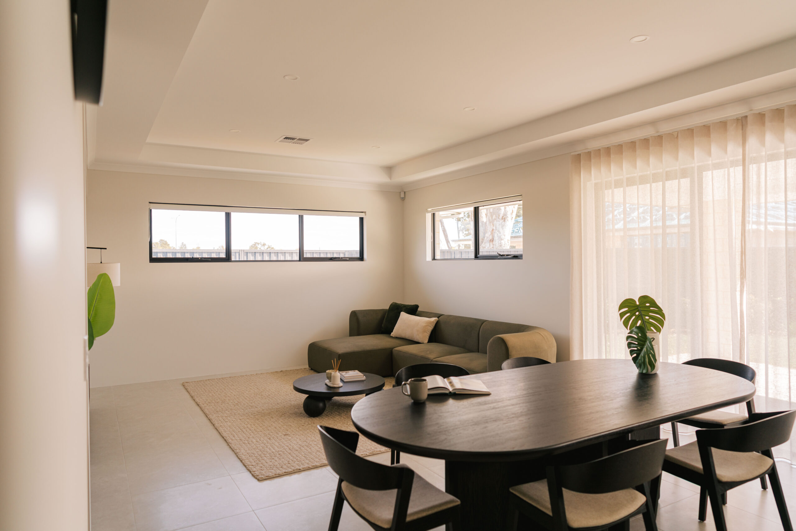 Modern living and dining area with a sectional sofa, oval dining table, and large windows.