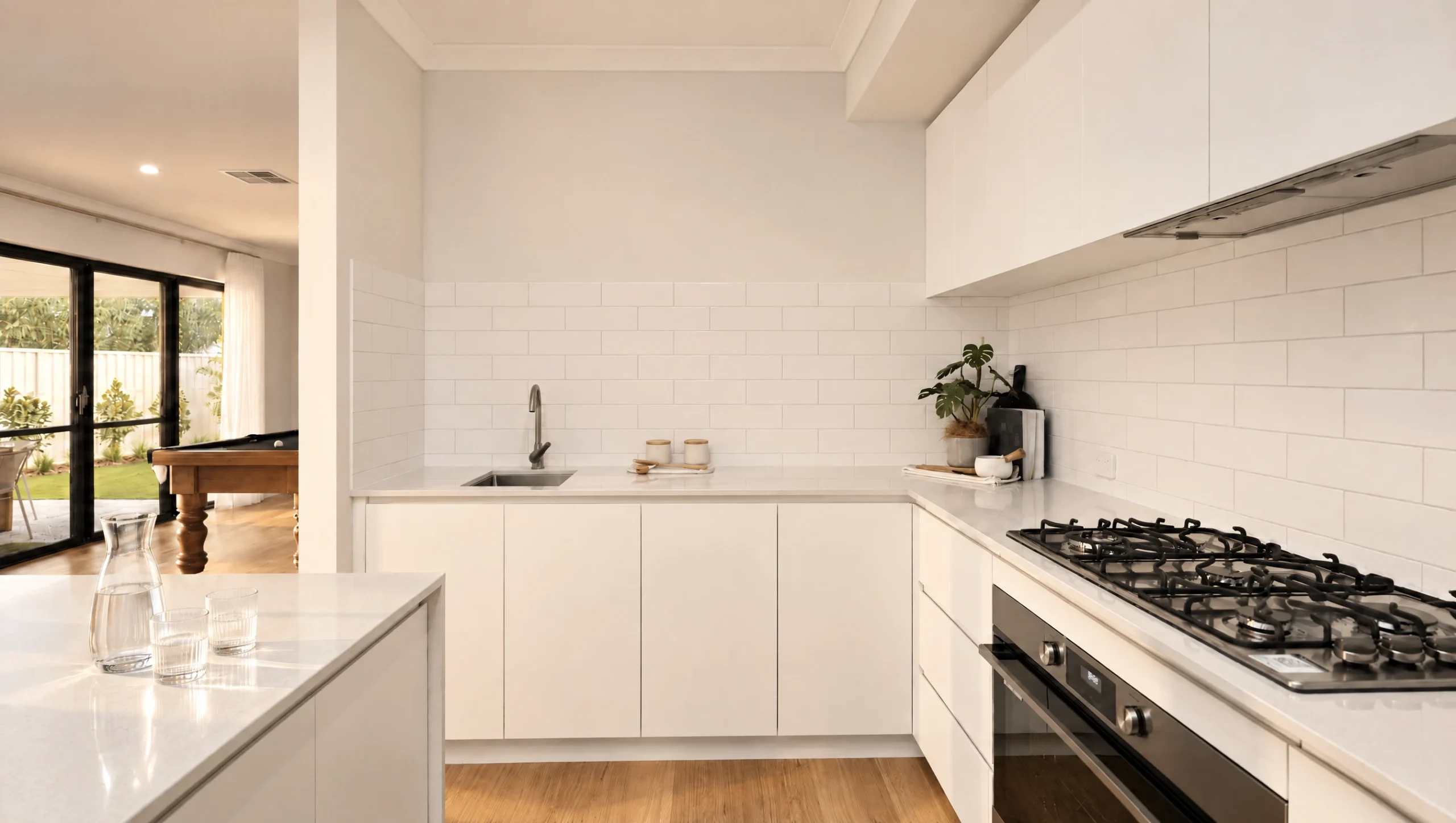 Modern white kitchen with a gas stovetop, sink, and view to a living area with a pool table.