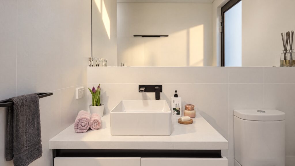 Modern bathroom vanity with a white vessel sink, black faucet, and decorative items, next to a toilet.