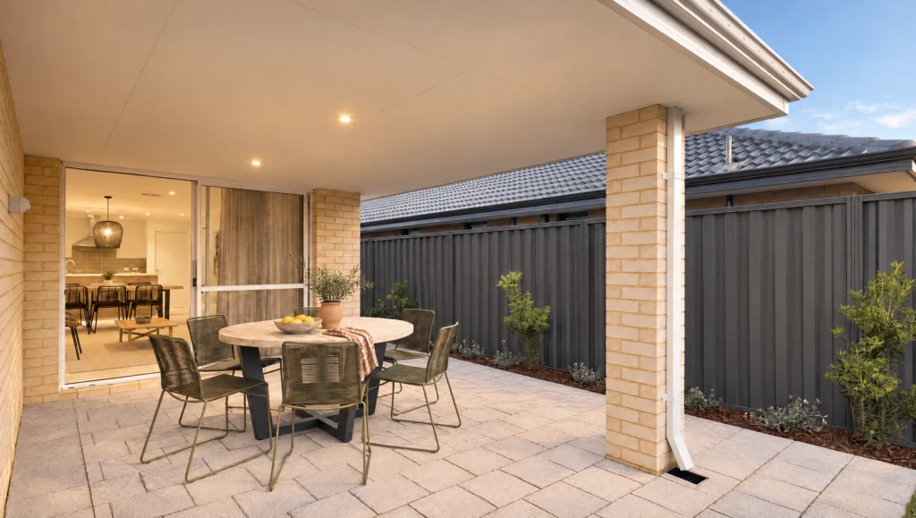 The Massey Bay alfresco area features a round table and chairs, with a view into the kitchen.