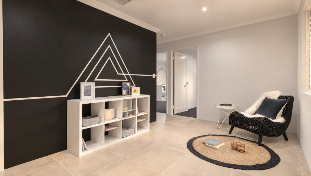 Modern nursery room with black accent wall featuring geometric white lines and a white shelving unit.