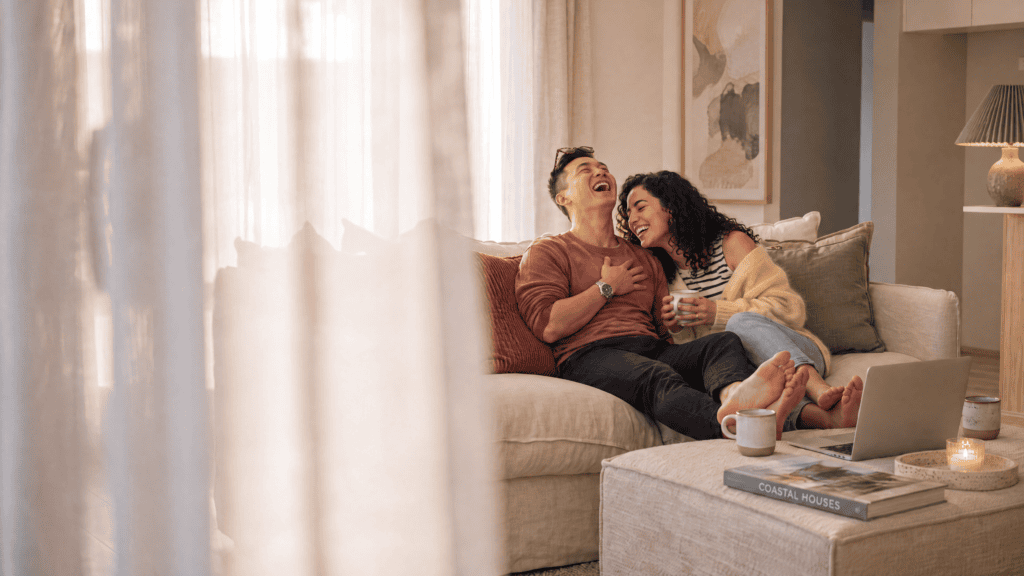 A couple laughs together on a couch, representing the confidence and happiness of building a home with New Homes WA.