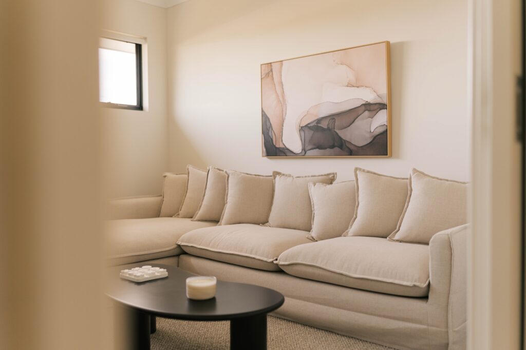 A large, neutral-toned sectional sofa with many cushions is arranged in a living room with abstract art above it.