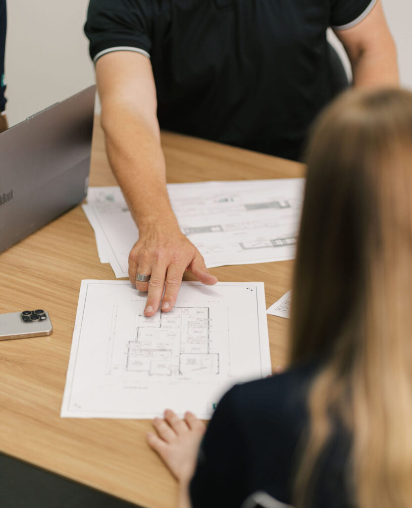 A New Homes WA representative points to a floor plan while discussing it with a client.