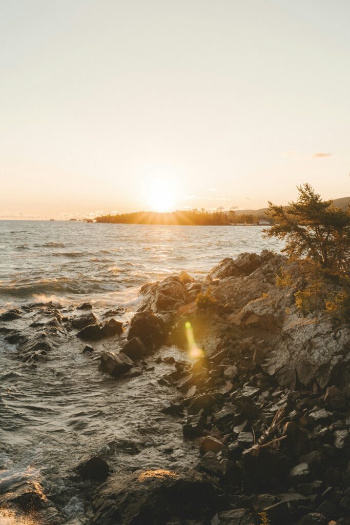 Sunset over a rocky coastline with gentle waves lapping the shore.