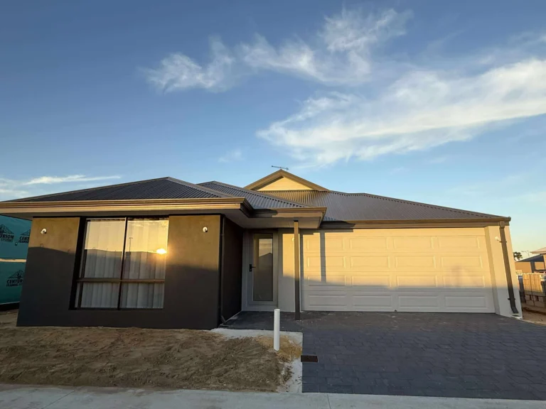 Modern dark grey house with a cream garage door and paved driveway at sunset.
