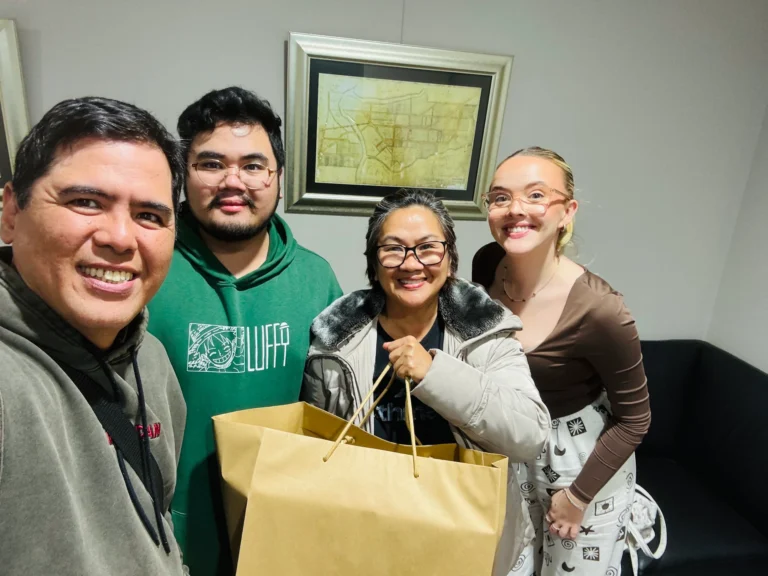 A family of four smiles for a selfie, holding a large gift bag.