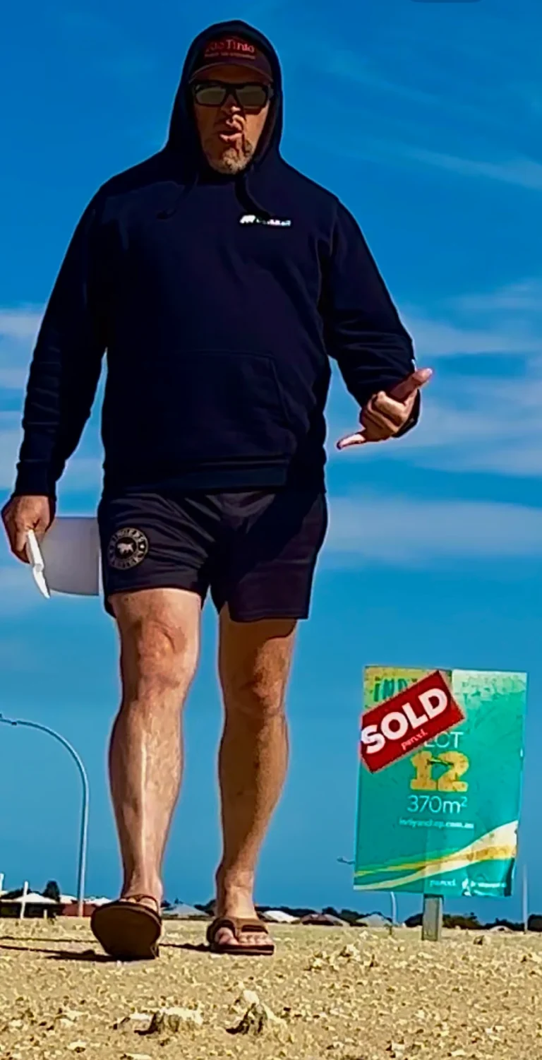 Man in hoodie and shorts walks past a sold sign for Lot 12, 370m².