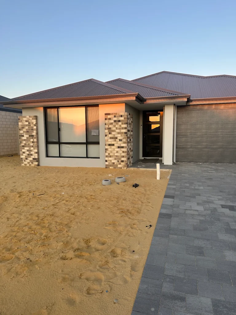 A modern house exterior with a grey roof, brick accents, and a paved driveway under a clear sky.