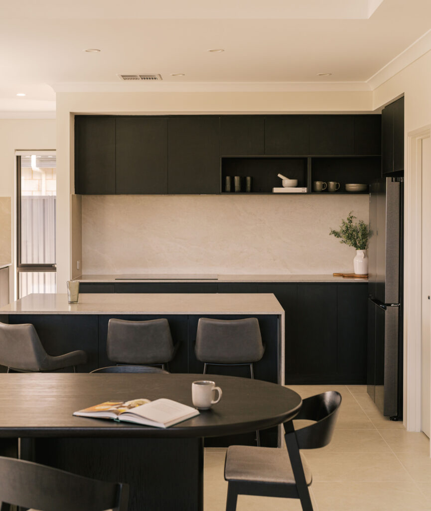Modern dark kitchen with island, bar stools, and dining table with open book and mug.