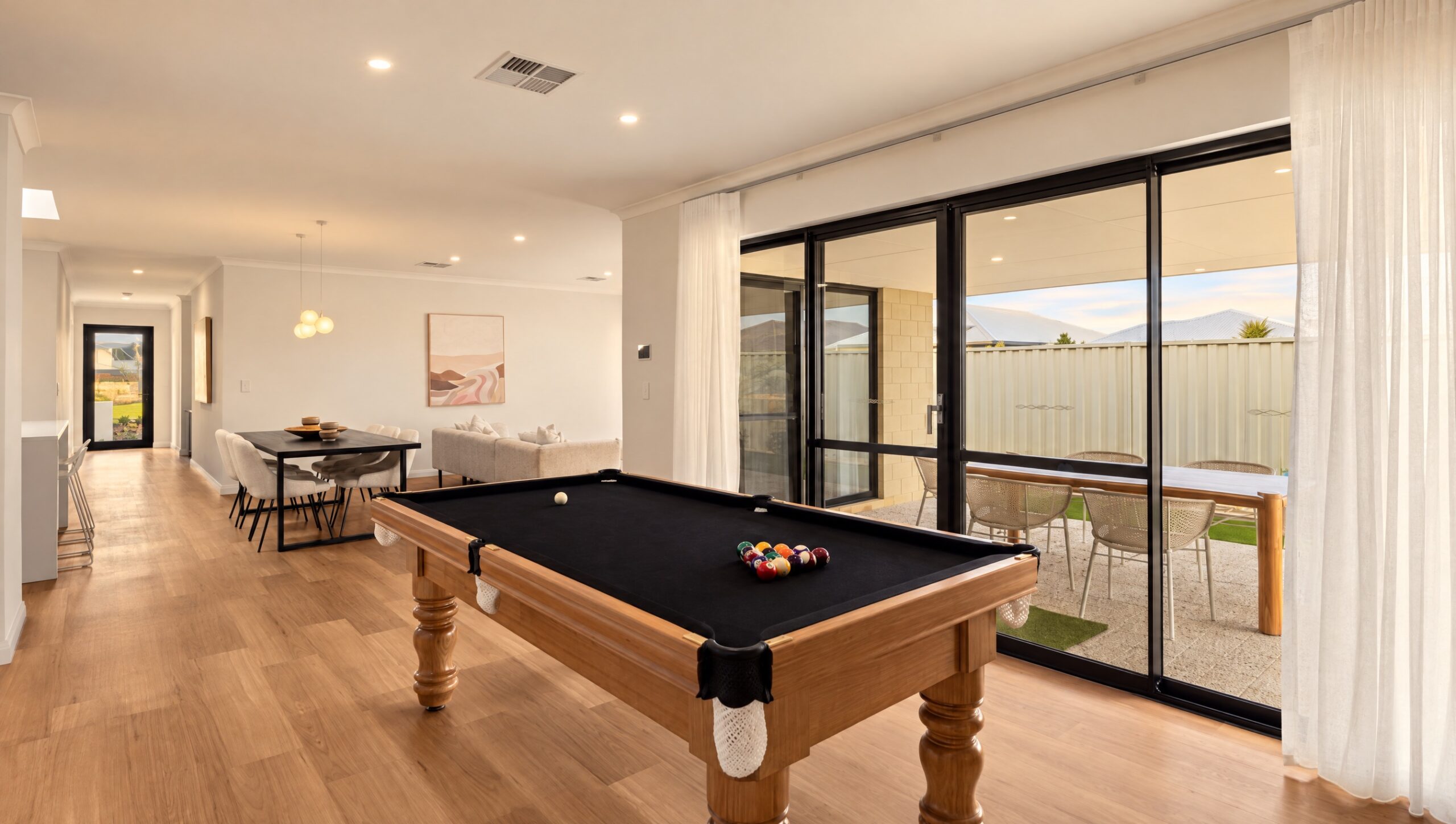 Modern open-plan living area with a pool table, dining set, and lounge, opening to an outdoor patio.